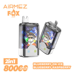 Two transparent-bodied AiRMEZ Fox disposable vapes on a white background, shown front and at an angle with colourful panels featuring a cartoon fox in a hat and sunglasses, orange AiRMEZ logo top-left and orange labels stating 2in1 800 puffs and flavours Blueberry on Ice / Blueberry Raspberry